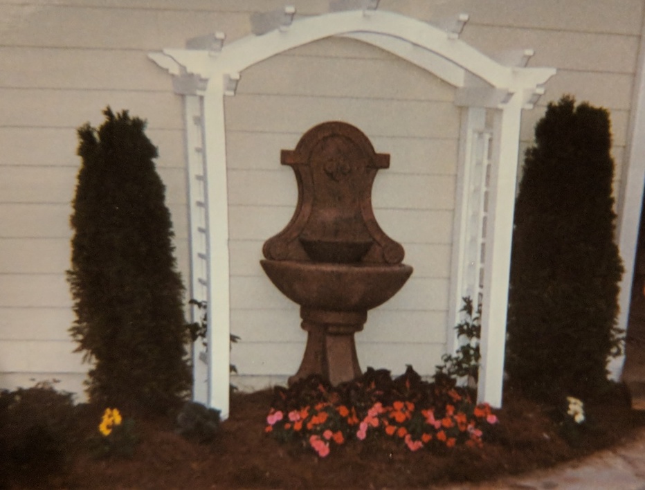 water fountain against house covered by an arbor of decorative wooden slats