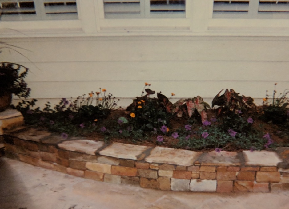 semicircular garden bed enclosed in wall of rock brickes with smooth rock plates on top