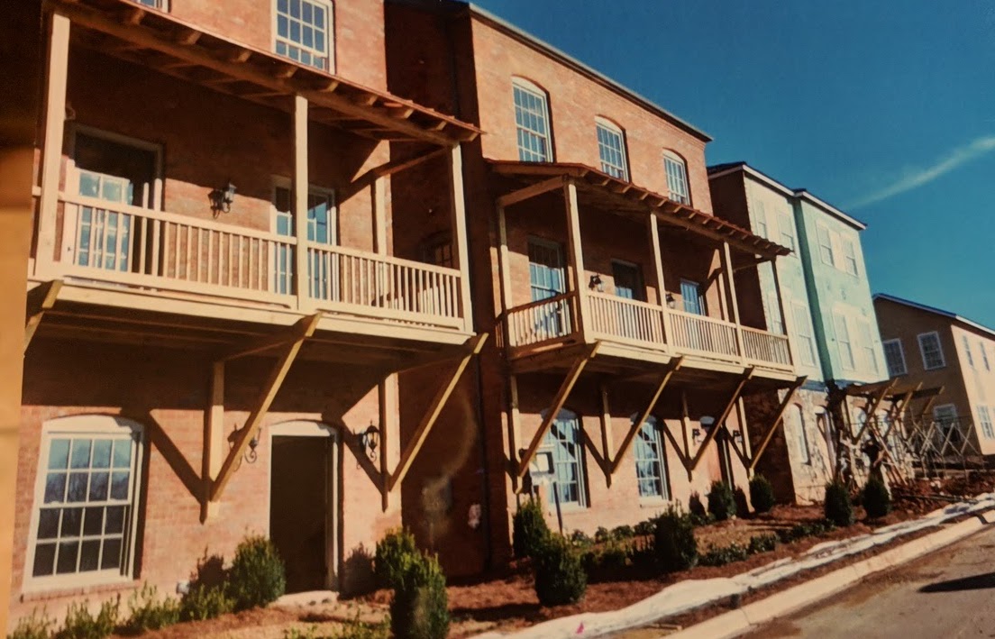 wooden porches with roofs, beams, and slatted wooden sides on outside the second stories of a row of townhouses, New Orleans style