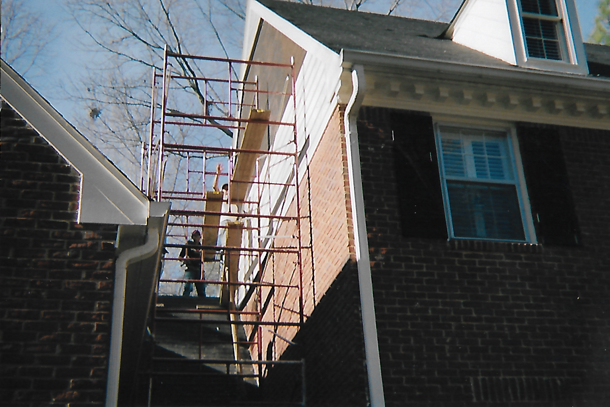 construction association working on scaffolding along the sides of a two-story house